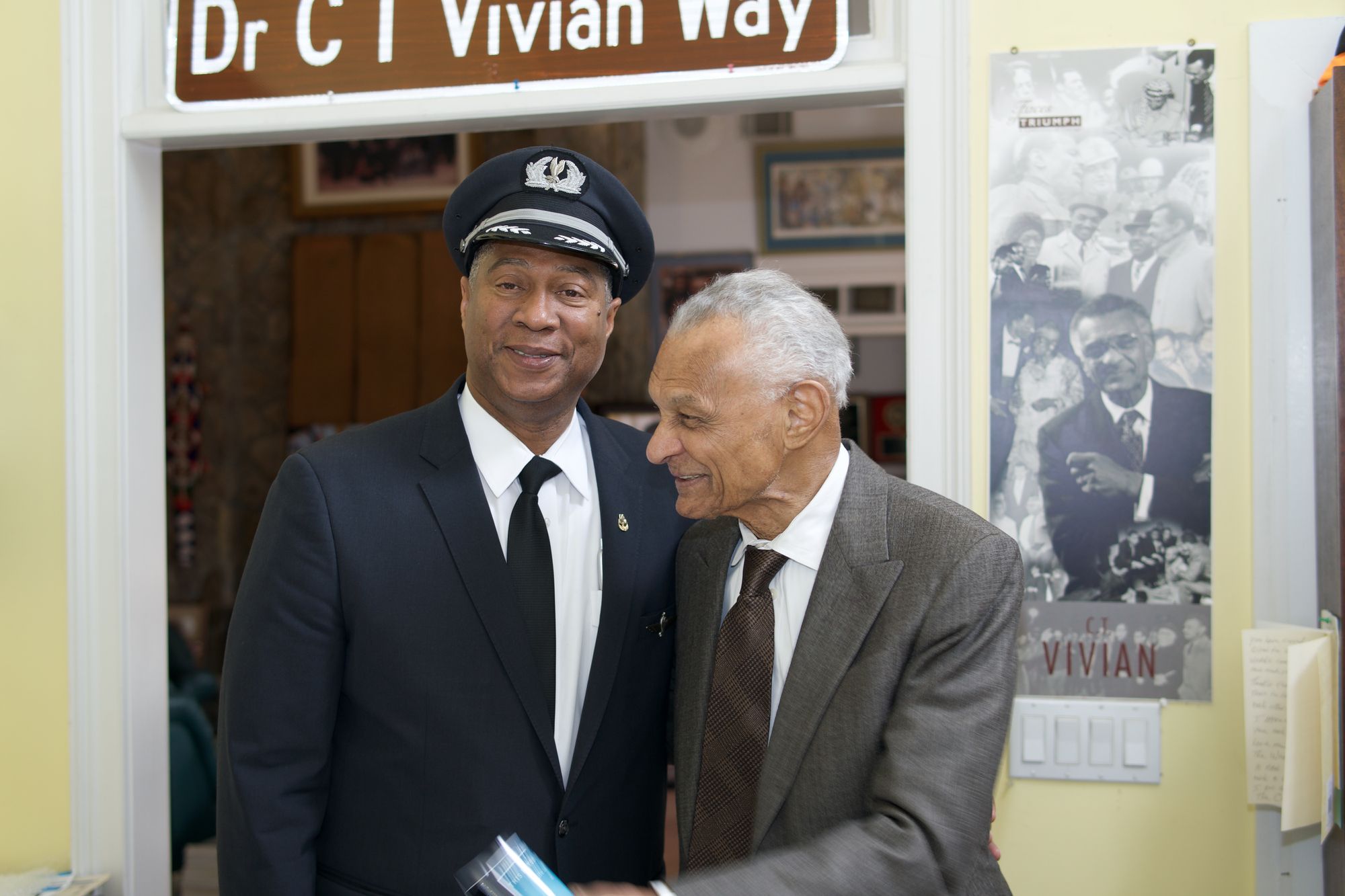 The Captain holding a copy of This Is Your Captain Speaking, with a mentor, in a room dedicated to Rev. Dr. C.T. Vivian